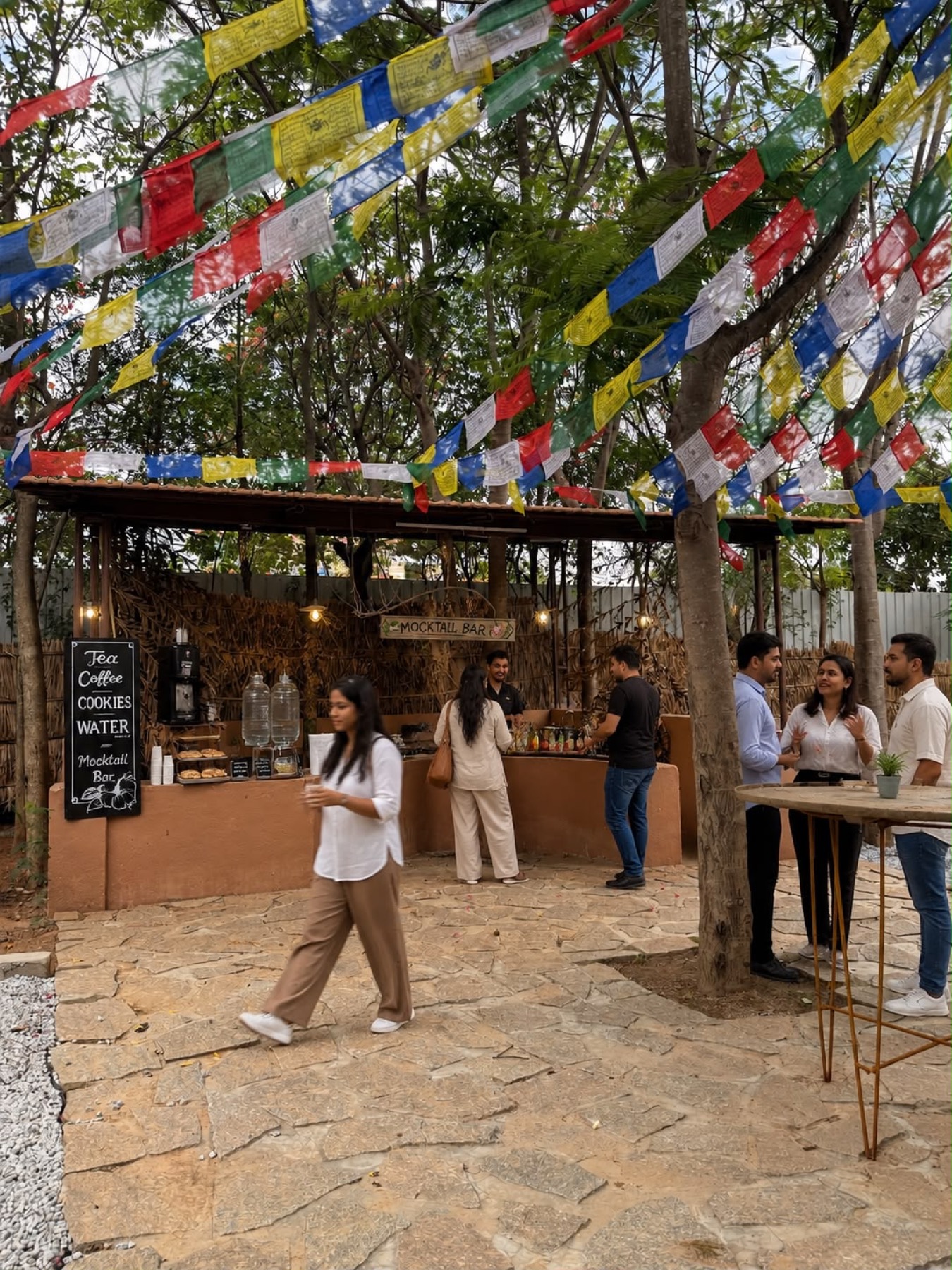 A team gathered at an outdoor coffee and refreshment counter under prayer flags at Orchid Tree